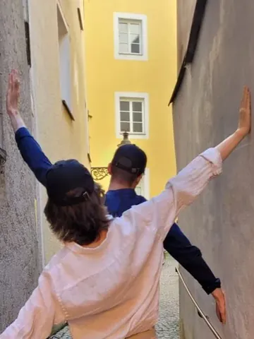 Zwei Spielende mit ausgebreiteten Armen in einer engen Passauer Gasse
