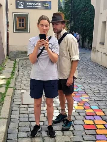 Zwei Spielende lesen auf dem Handy das nächste Rätsel, auf den bemalten Pflastersteinen der Höllgasse in Passau